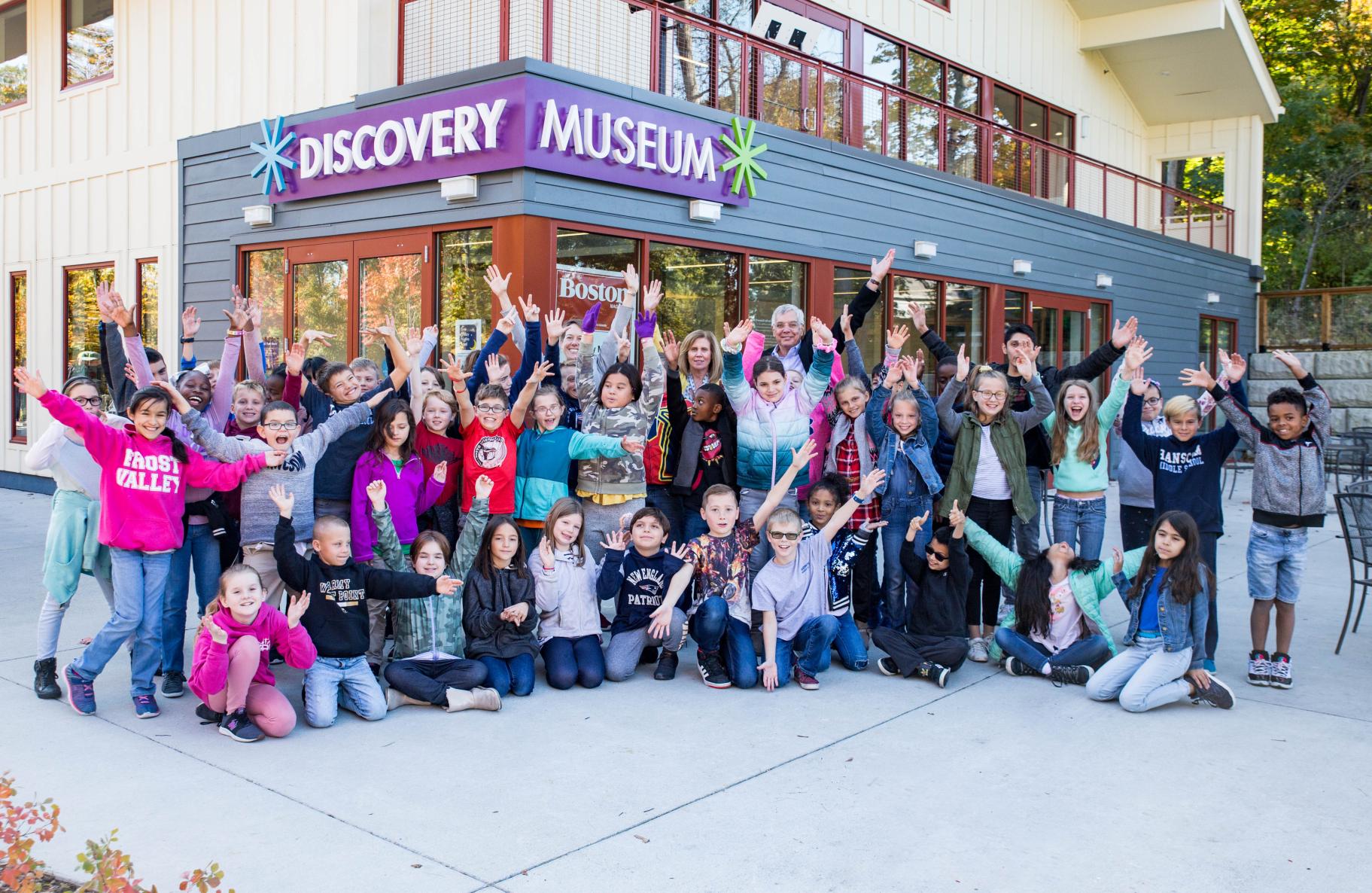 a big group of excited students stand in front of the Discovery Museum